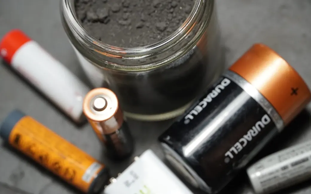 Assorted battery types beside a jar of recovered black mass